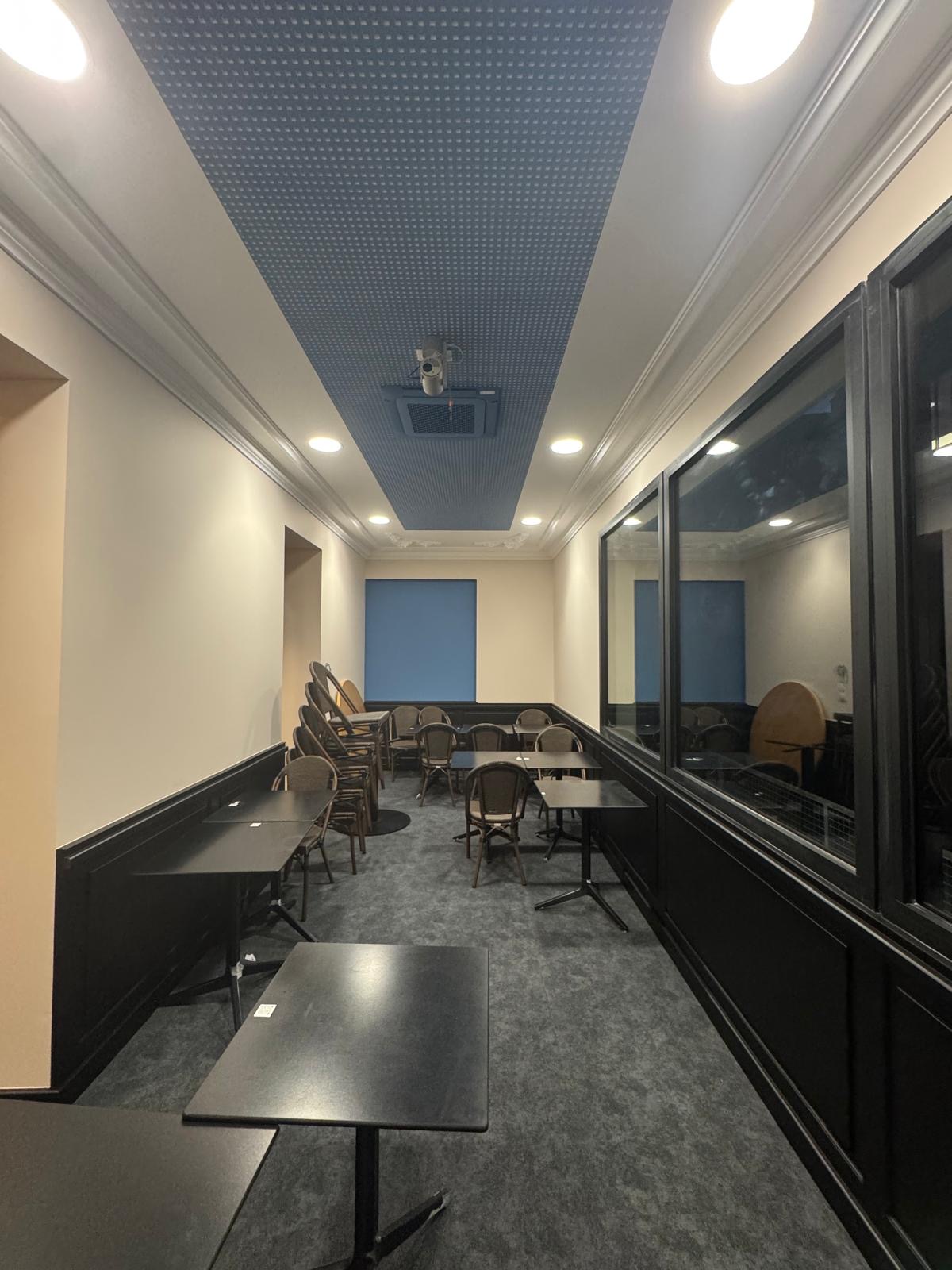 Plafond acoustique avec panneaux perforés et éclairage intégré, améliorant le confort sonore de la pièce.