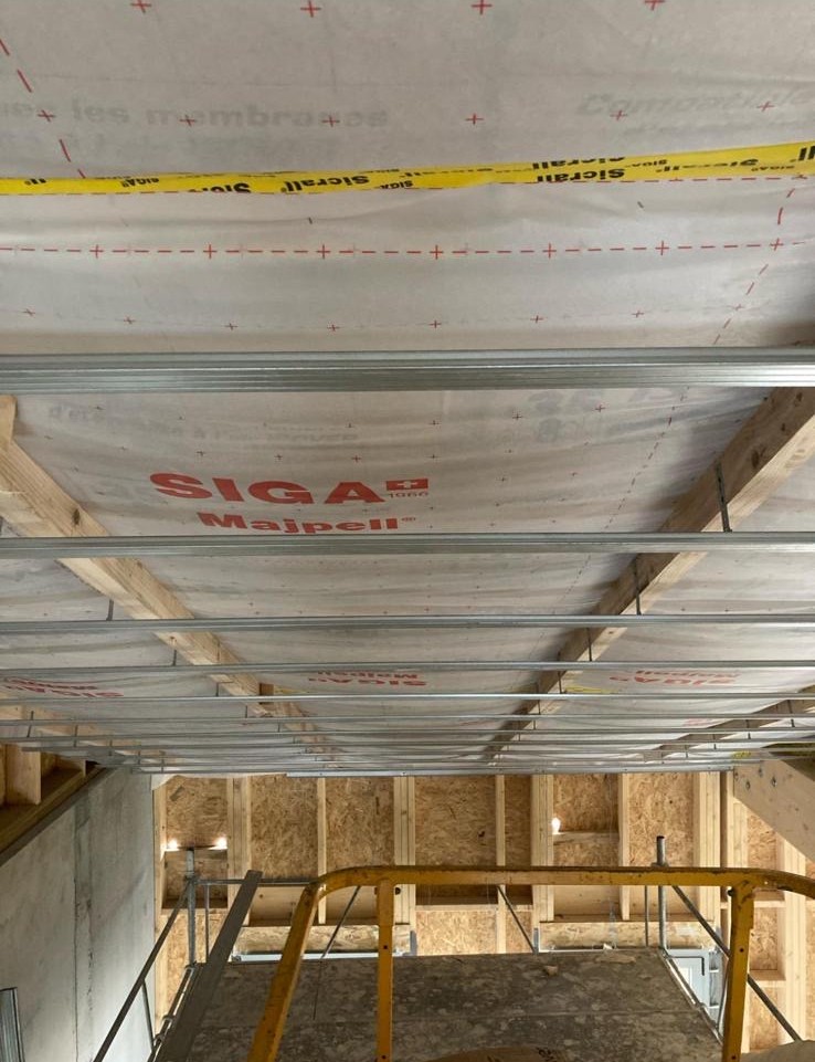 Membrane d’étanchéité à l’air posée sous plancher bois, avec ossature métallique pour plafond et suspentes fixées sur la structure.